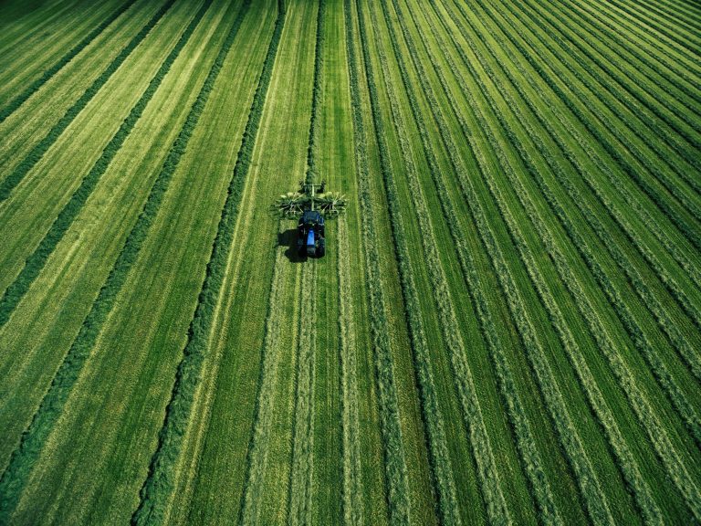 Blue tractor mowing green field, aerial view